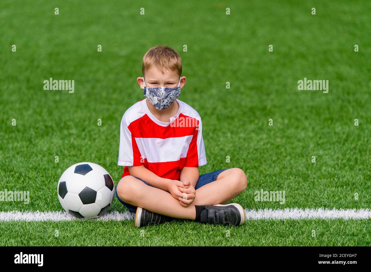 Bambino di scuola con maschera e palla in una lezione di educazione fisica. Ritorno sicuro a scuola durante il concetto pandemico. Distanza sociale per combattere COVID-19 Foto Stock