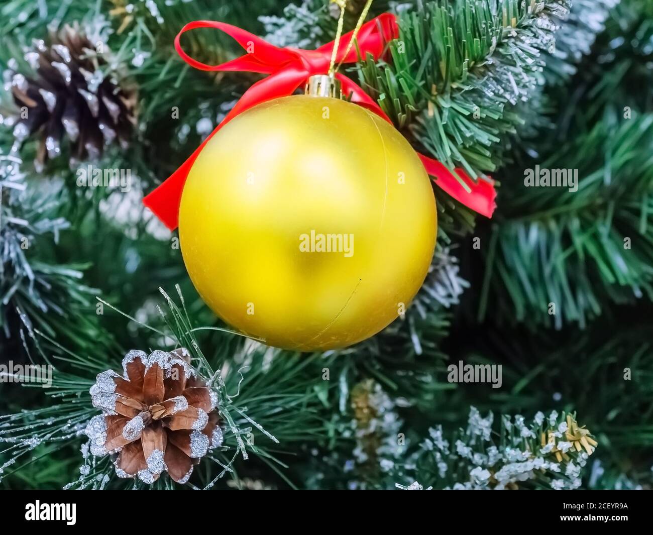 Sfera dorata opaca di natale appesa su ramo di pino artificiale con coni reali Foto Stock
