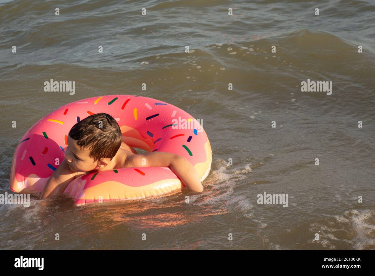 Un ragazzo di 5 anni nuota in mare, si rallegra e si diverte in un anello gonfiabile a forma di ciambella. Foto Stock