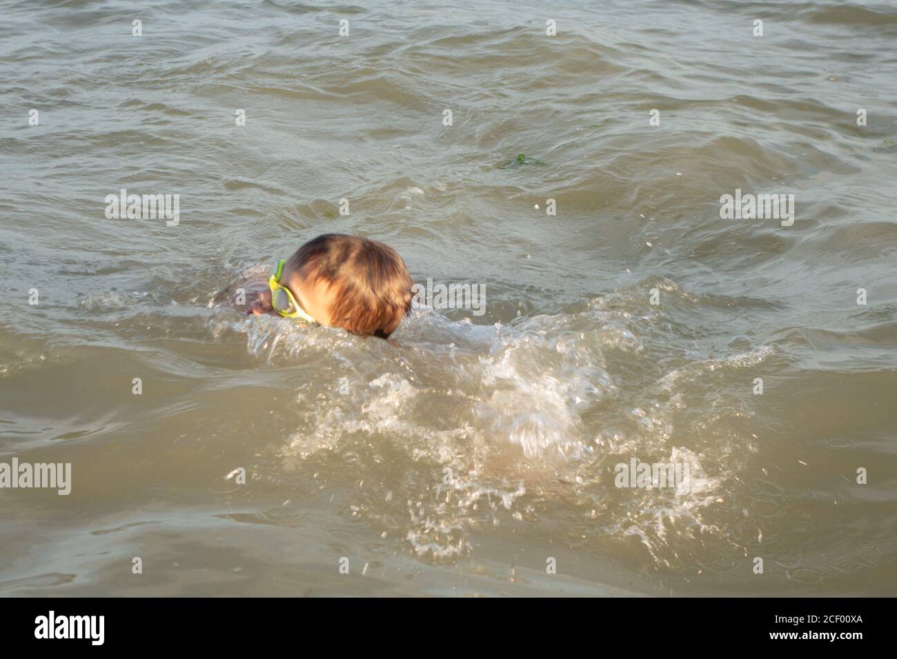 Un ragazzo di 10 anni in occhiali da bagno verdi nuota in mare vicino alla riva. Foto Stock