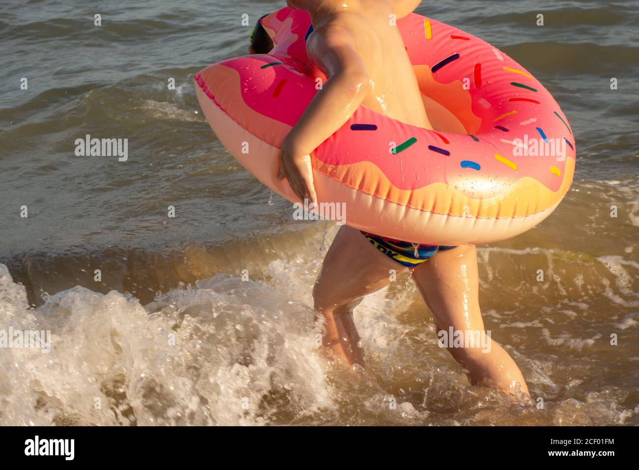 Un ragazzo di 5 anni nuota in mare, si rallegra e si diverte in un anello gonfiabile a forma di ciambella. Foto Stock