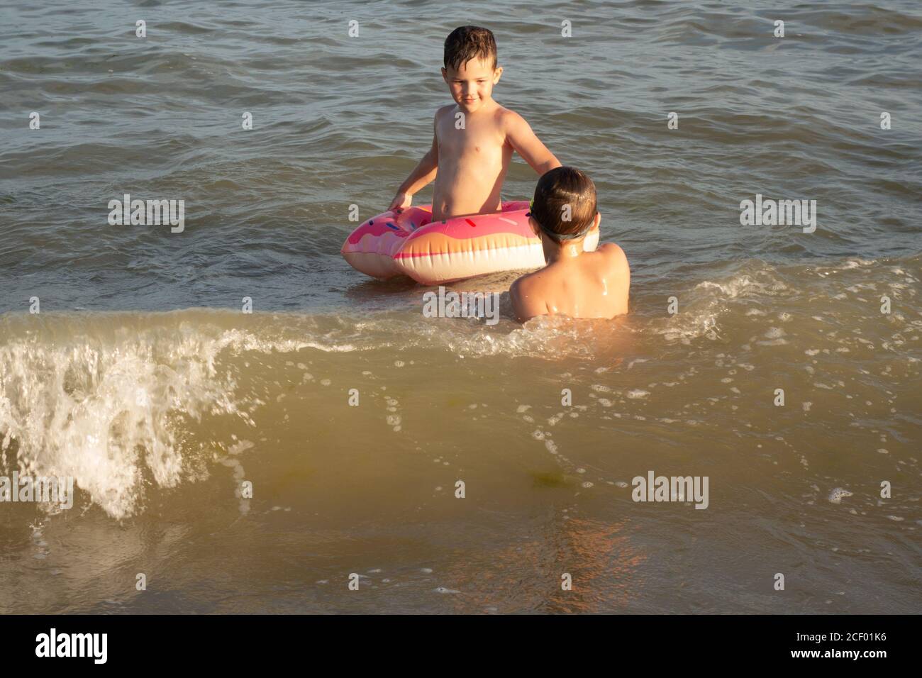 Due fratelli di 5 e 10 anni nuotano e si divertono in mare in una giornata di sole limpida. Foto Stock