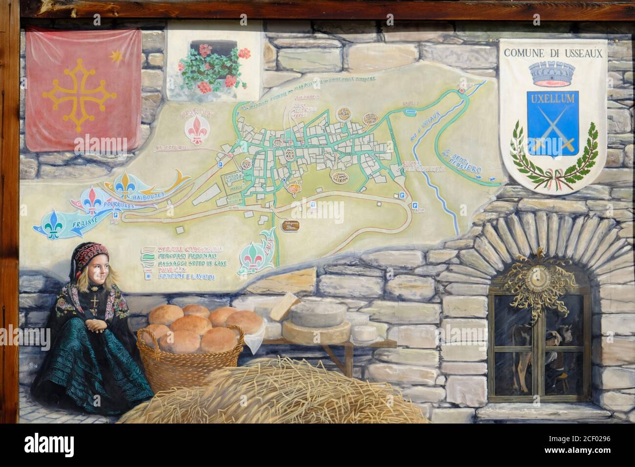 Murale dipinto di una giovane ragazza in costume tradizionale di montagna accanto ad un cesto di pane fresco e di formaggi tondi nel piccolo villaggio di Usseaux, Piemon Foto Stock