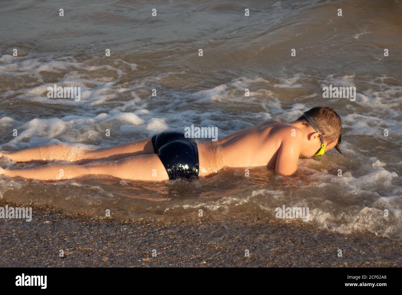 Un ragazzo di 10 anni in occhiali da bagno verdi nuota in mare vicino alla riva. Foto Stock