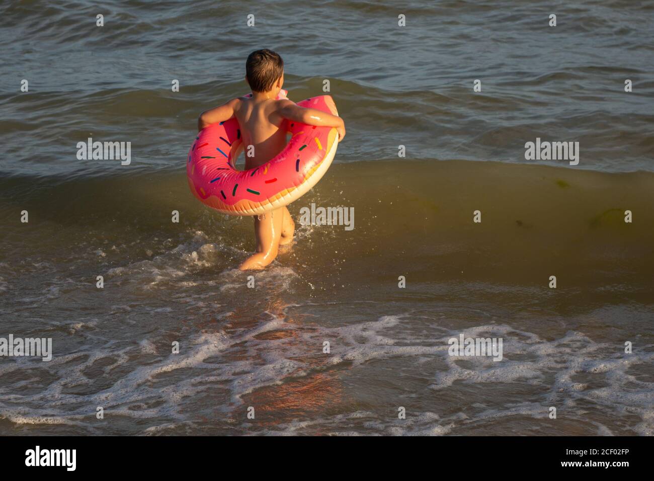 Un ragazzo di 5 anni nuota in mare, si rallegra e si diverte in un anello gonfiabile a forma di ciambella. Foto Stock