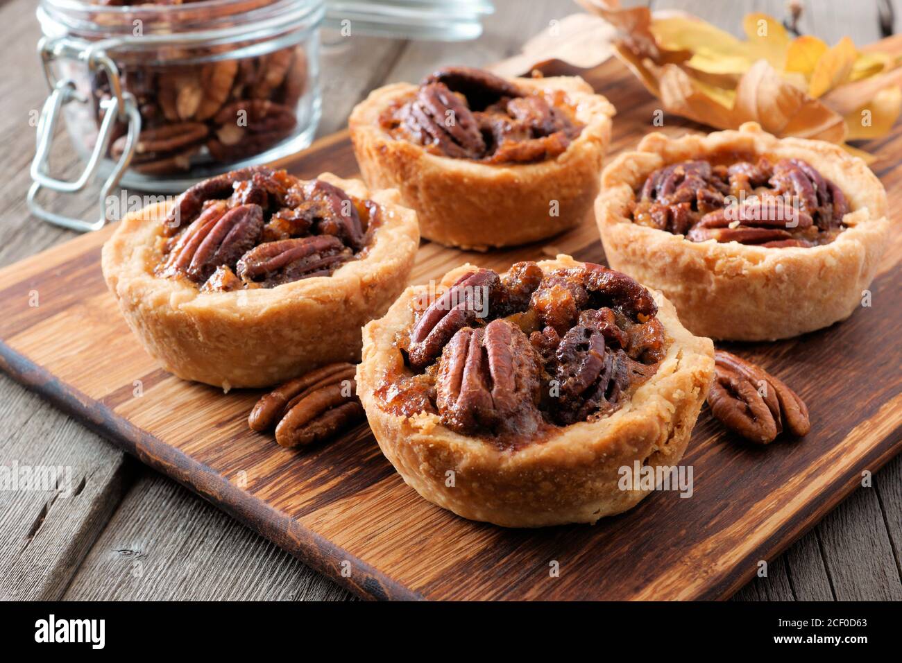 Mini crostate di torta di pecan, primo piano di scena su un server di legno su uno sfondo rustico di legno Foto Stock