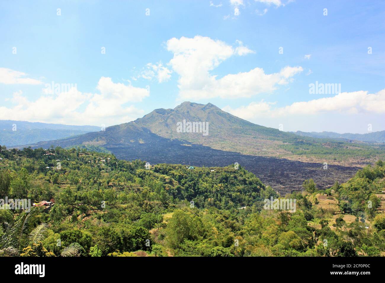 Monte Batur Vulcano, con alberi e foglie verdi in primo piano e campo di roccia vulcanica nera a Bali, Indonesia Foto Stock