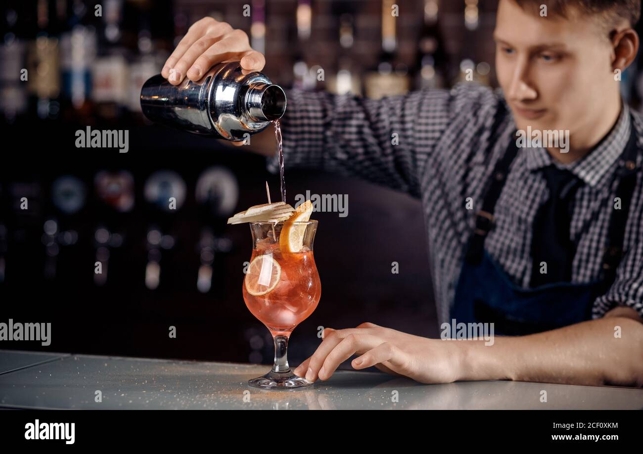 Il barman prepara un cocktail in shaker con alcol e ghiaccio. Barman sfondo scuro Foto Stock
