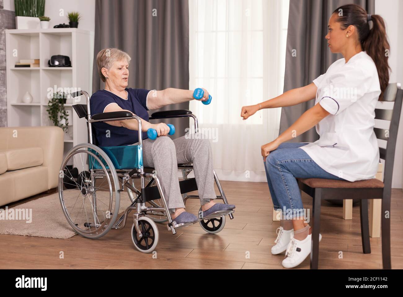 Donna anziana in sedia a rotelle che fa riabilitazione con pesi. Disabile anziano ricoverato infermiera di aiuto professionale, cura di casa di riposo e riabilitazione Foto Stock