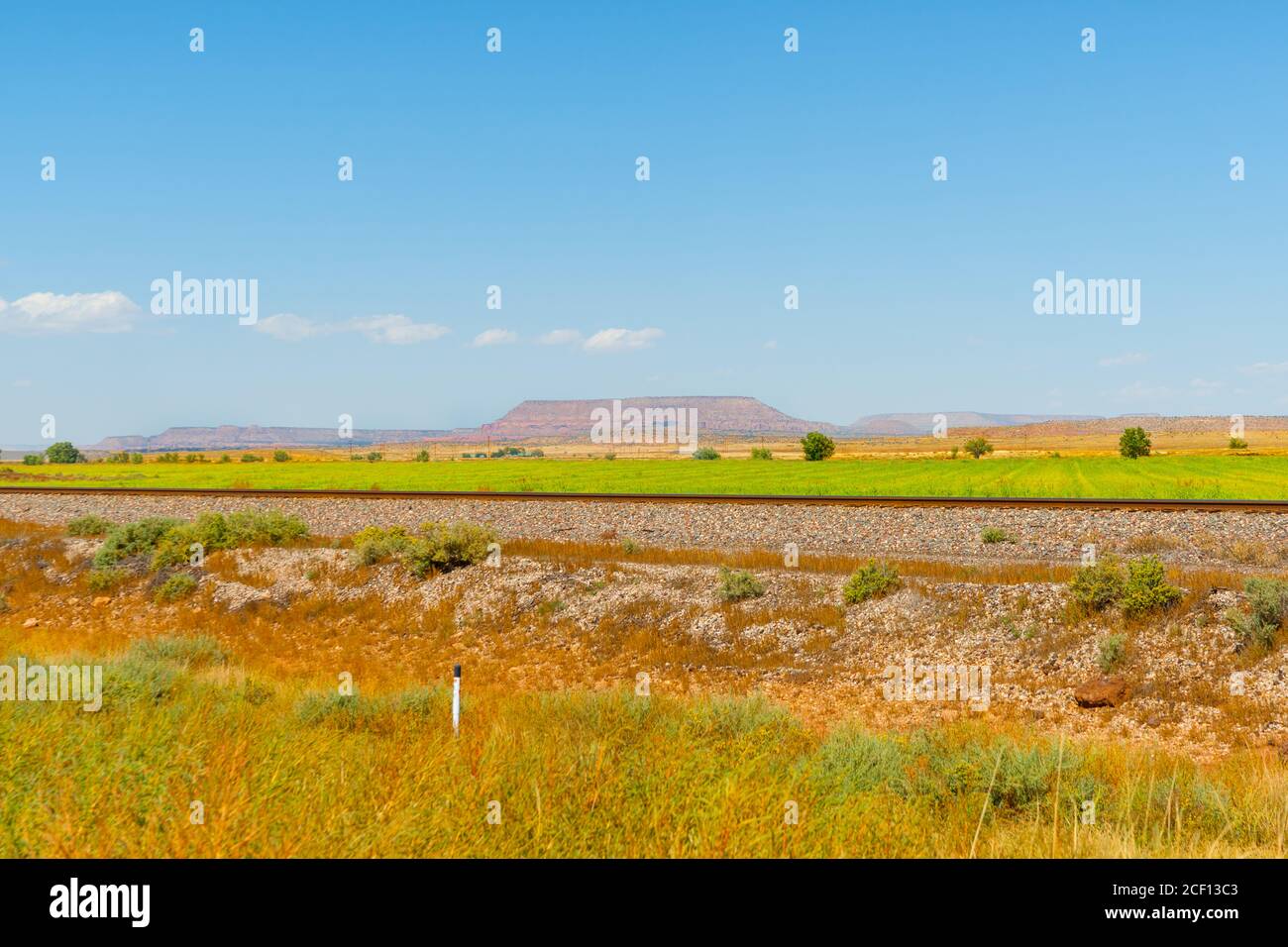 Pianure pianeggianti del New Mexico con lontane pianure mesa in lontananza e binari ferroviari in primo piano sotto il cielo blu. Foto Stock