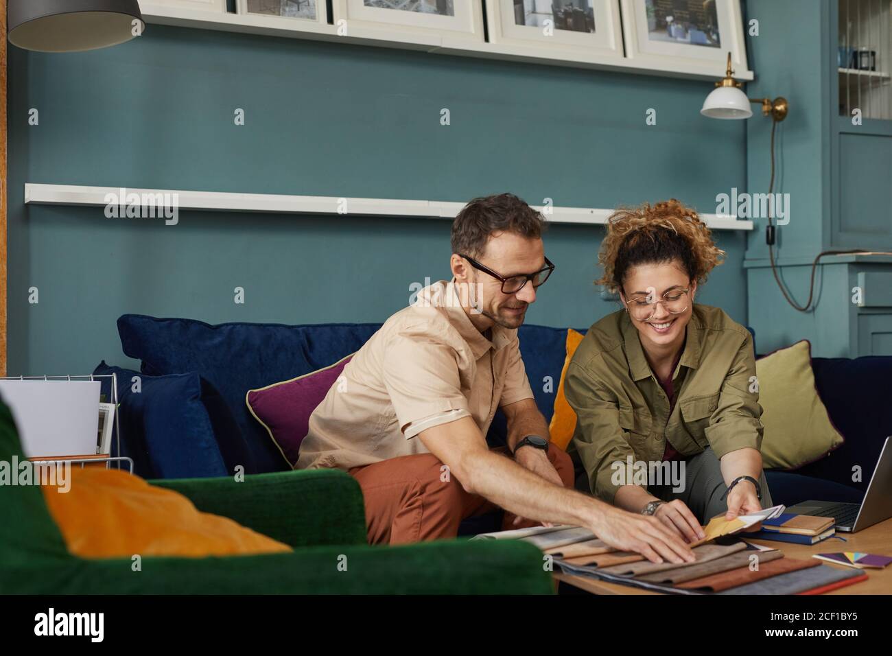 Due stilisti di moda seduti sul divano e che esaminano la nuova collezione di campioni di tessuto di moda in ufficio moderno Foto Stock