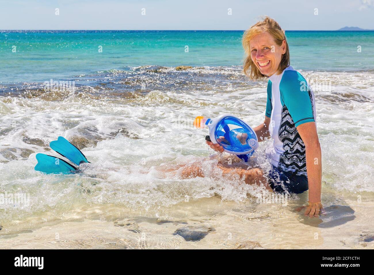 Donna caucasica seduta in acqua di mare con maschera da snorkeling e. alette Foto Stock