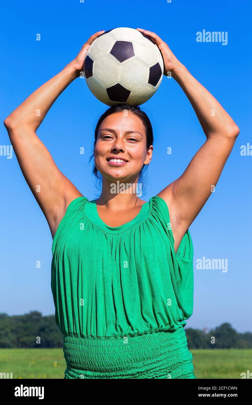 Giovane donna colombiana che tiene il calcio in testa nel cielo blu Foto Stock