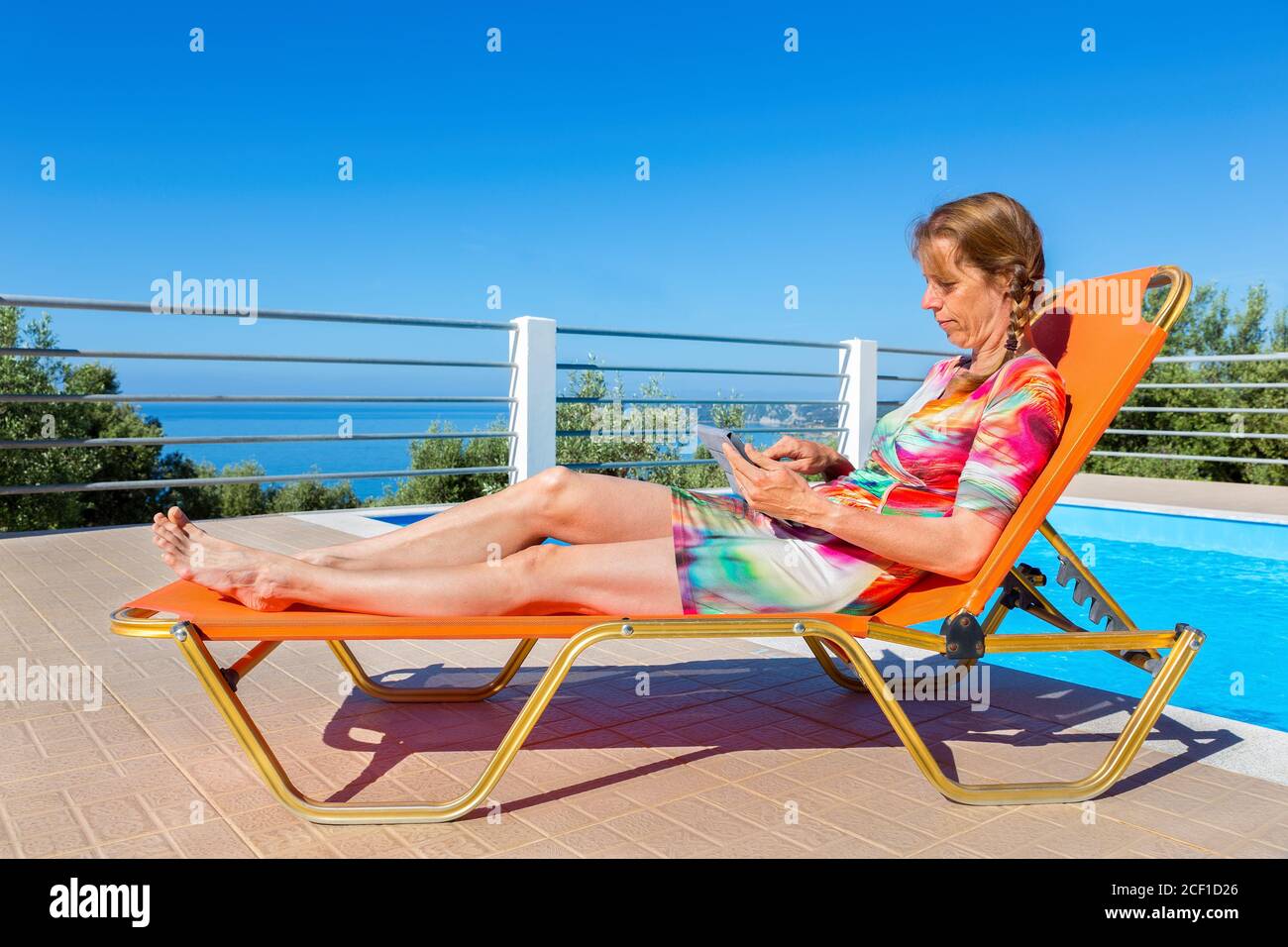 Donna olandese di mezza età sdraiata su una tavoletta da lettura arancione vicino alla piscina Foto Stock