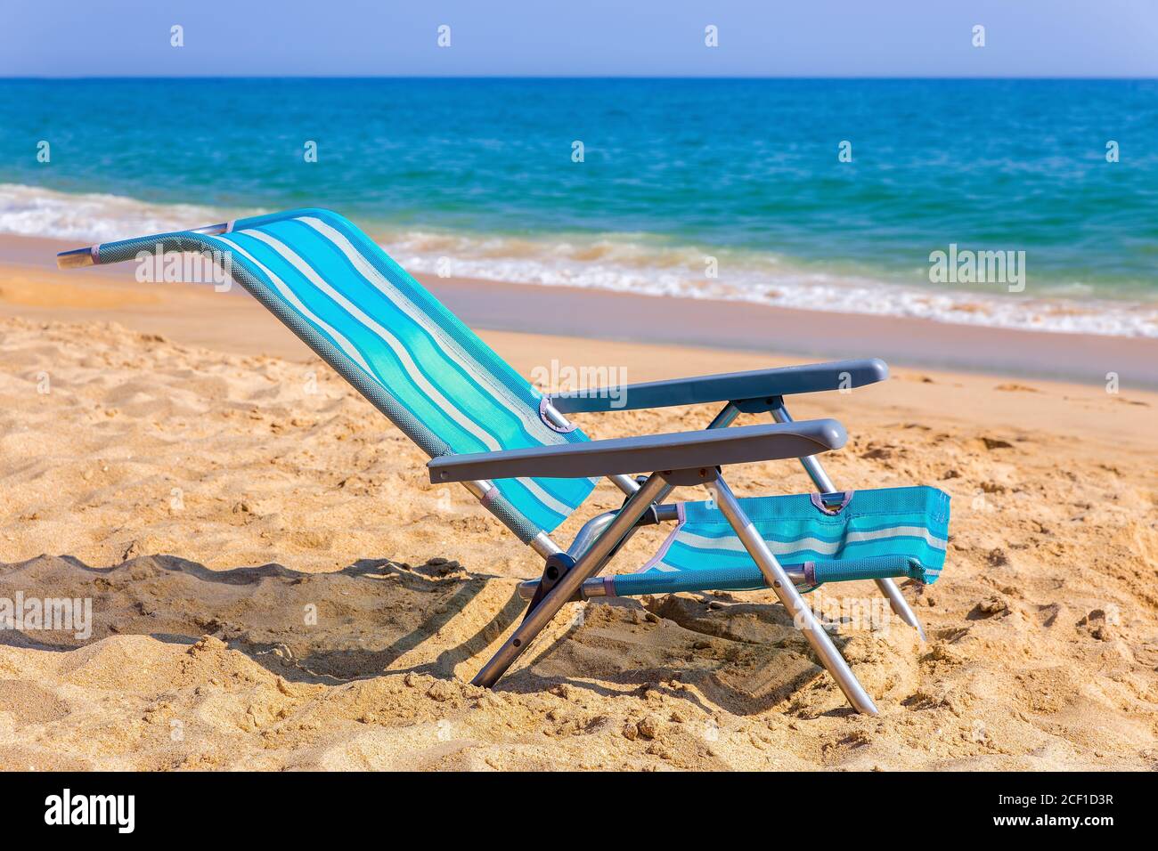 Una sedia da spiaggia blu sulla costa di Albufeira con mare Foto Stock