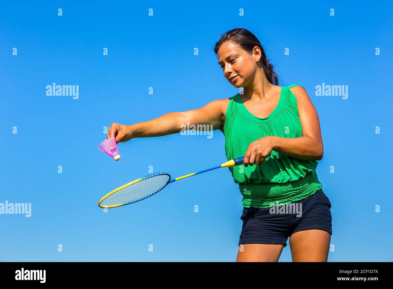 Giovane donna colombiana serve con racchetta di badminton e navetta in parte anteriore del cielo blu Foto Stock