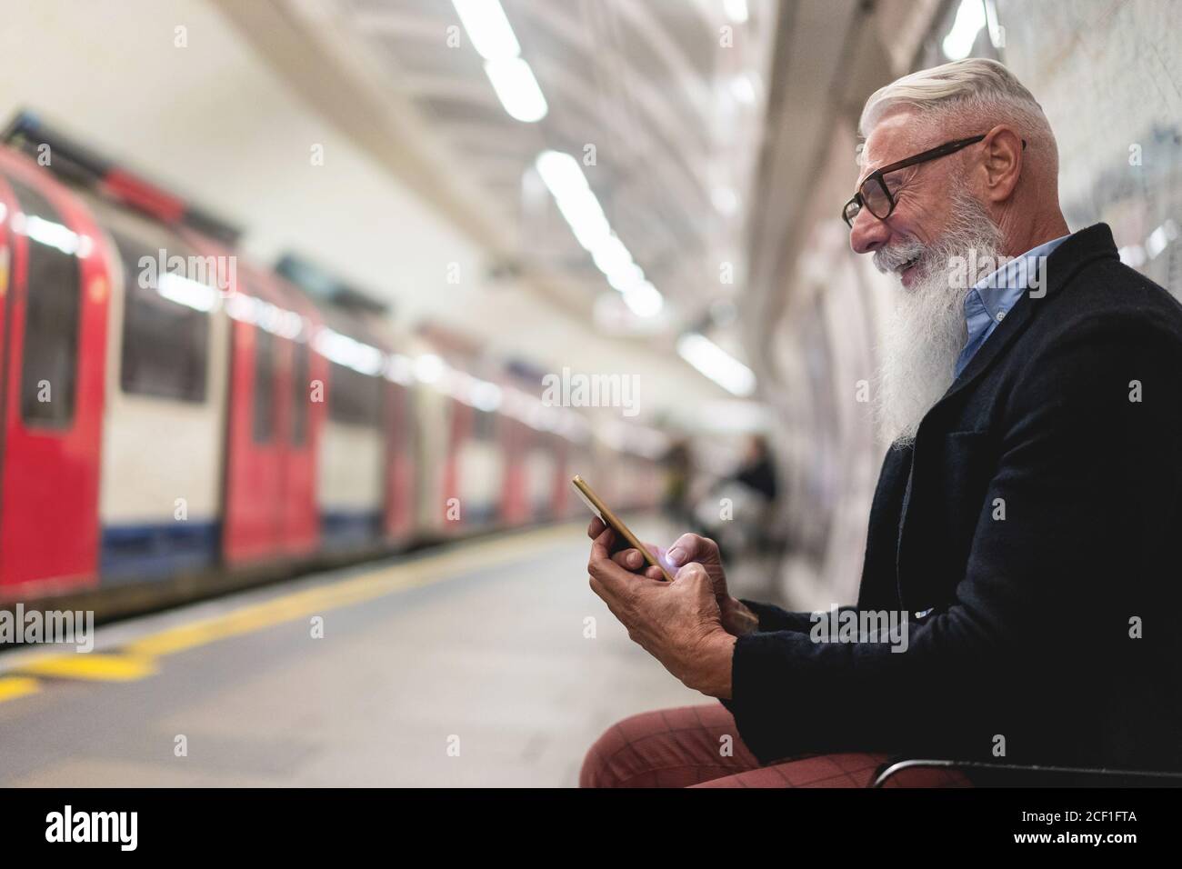 Hipster uomo anziano che chiacchiera sul suo smartphone mentre aspetta Treno della metropolitana - uomo maturo che si diverte con le tendenze tecnologiche - Tech anziani gioiosa notte Foto Stock