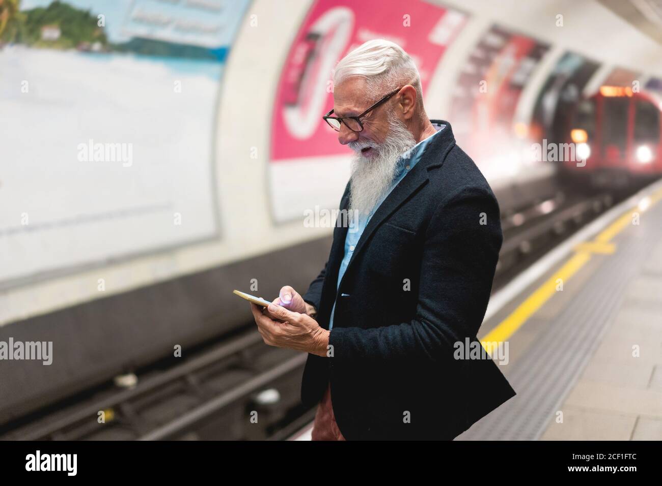 Hipster uomo anziano che chiacchiera sul suo smartphone mentre aspetta Treno della metropolitana - uomo maturo che si diverte con le tendenze tecnologiche - Tech anziani gioiosa notte Foto Stock