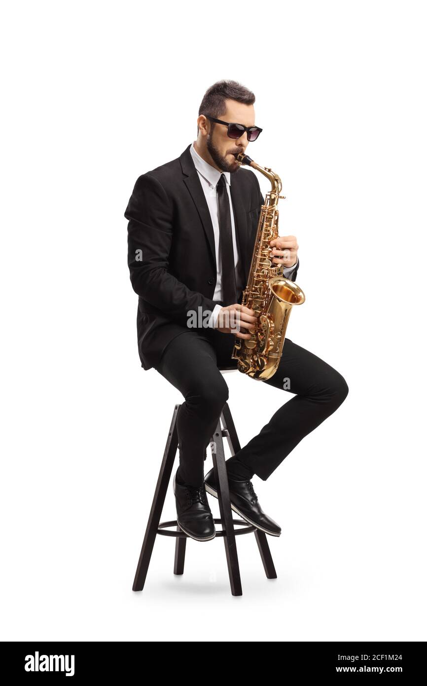 Musicista maschile in una tuta nera che suona un sassofono e. seduta su una sedia isolata su sfondo bianco Foto Stock