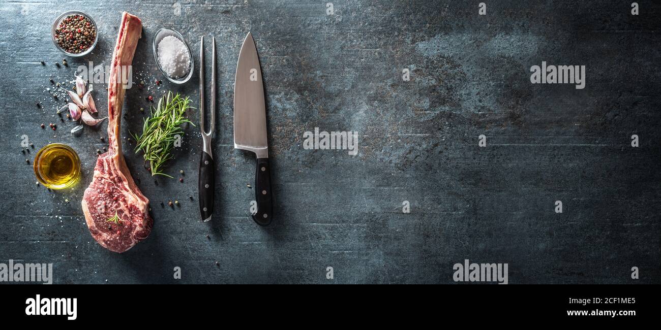 Bistecca di tomahawk cruda con coltello a forchetta sale spezie aglio e. Erbe su una vecchia tavola rustica - Vista dall'alto Foto Stock