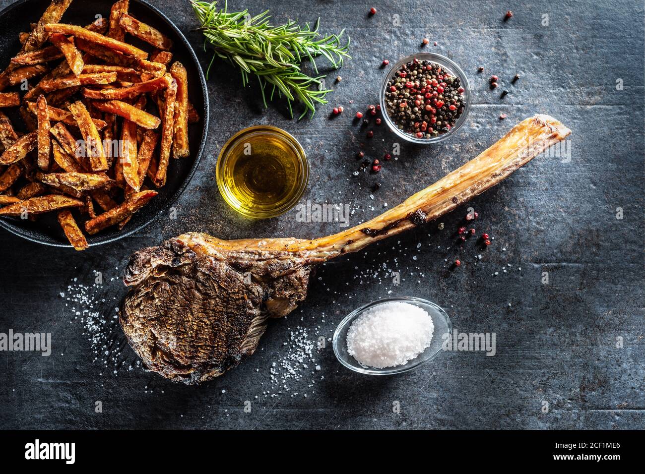 Bistecca di manzo tomahawk alla griglia con patate dolci fritte spezie al sale olio d'oliva e rosmarino su tavola rustica - cima di visualizza Foto Stock