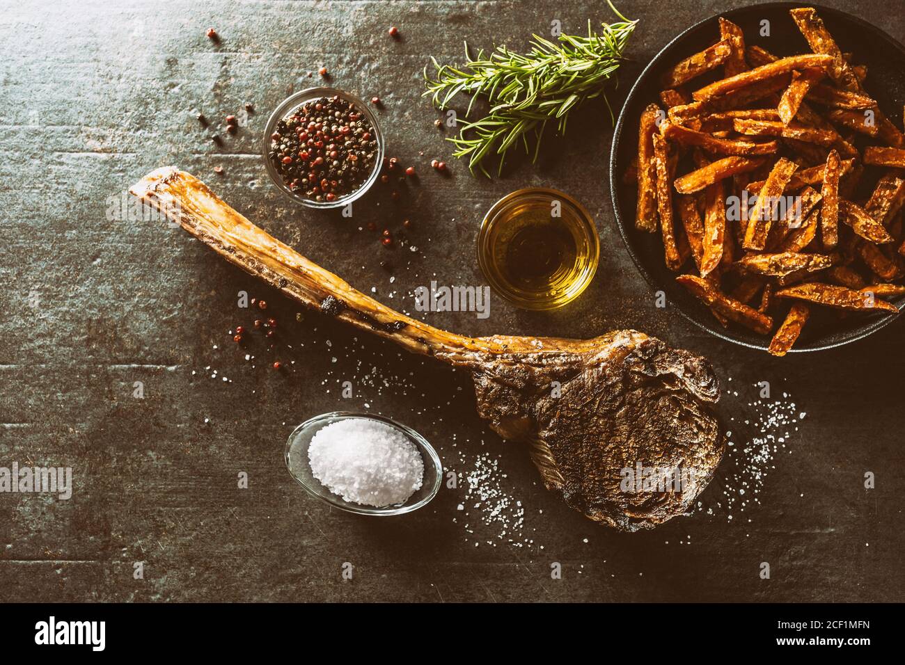 Bistecca di manzo tomahawk alla griglia con patate dolci fritte spezie al sale olio d'oliva e rosmarino su tavola rustica - cima di visualizza Foto Stock