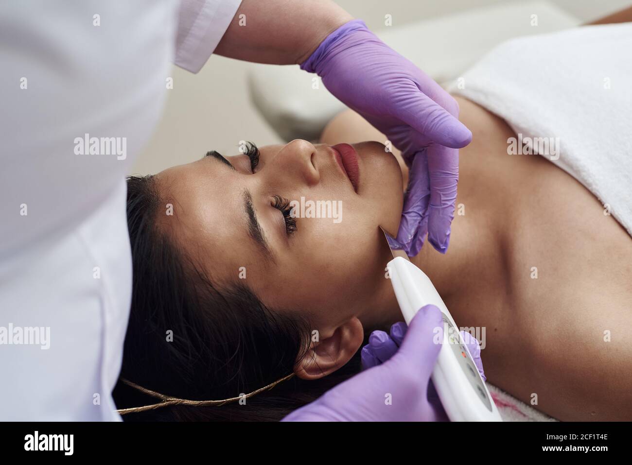 Donna che riceve la terapia di pulizia con un'apparecchiatura professionale ultrasonica in ufficio di cosmetologia. Procedura di pulizia a ultrasuoni del viso. Clinica cosmetologica. Foto Stock