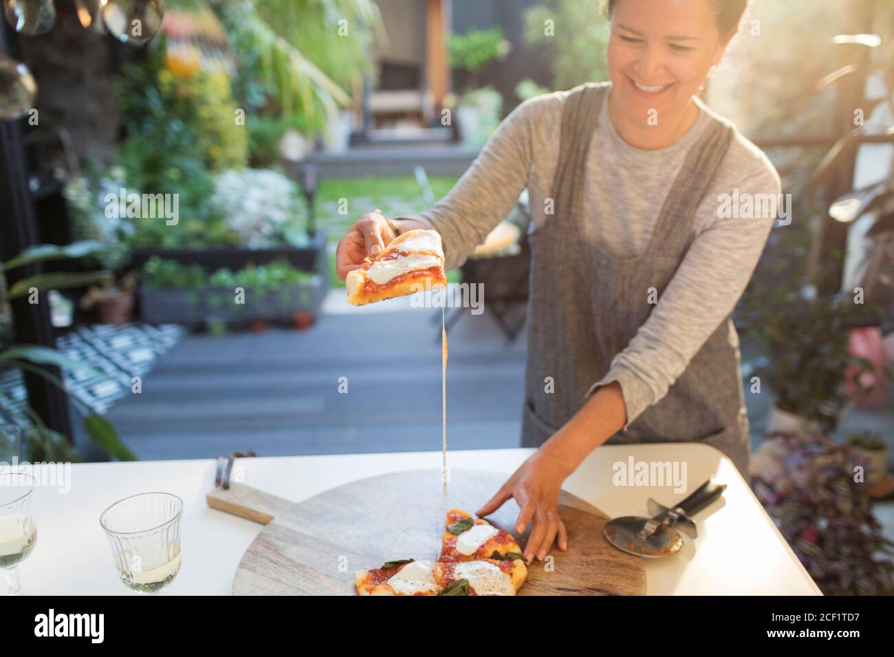 Donna sorridente che mangia pizza fatta in casa sul patio Foto Stock