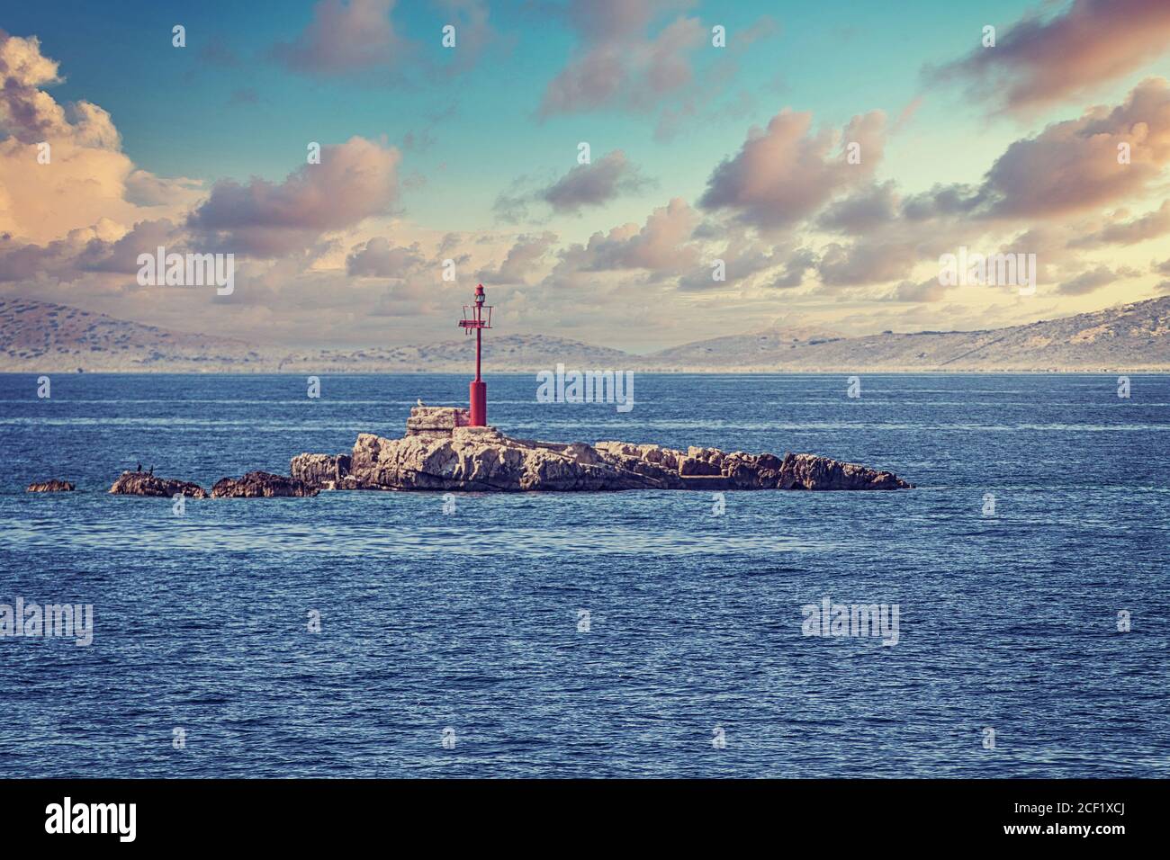Affioramenti rocciosi sulla linea d'acqua con un faro di soccorso all'arcipelago di Kornati, lontano dalla costa dalmata della Croazia. Foto Stock