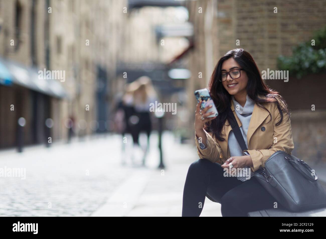 Donna d'affari sorridente che usa lo smartphone sul marciapiede della città Foto Stock