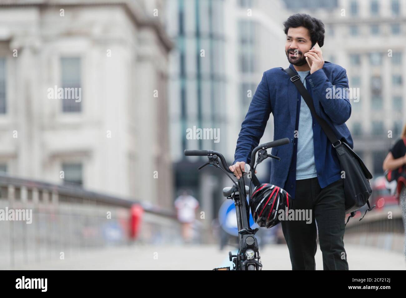 Uomo d'affari con bicicletta che parla su smartphone sul ponte della città Foto Stock