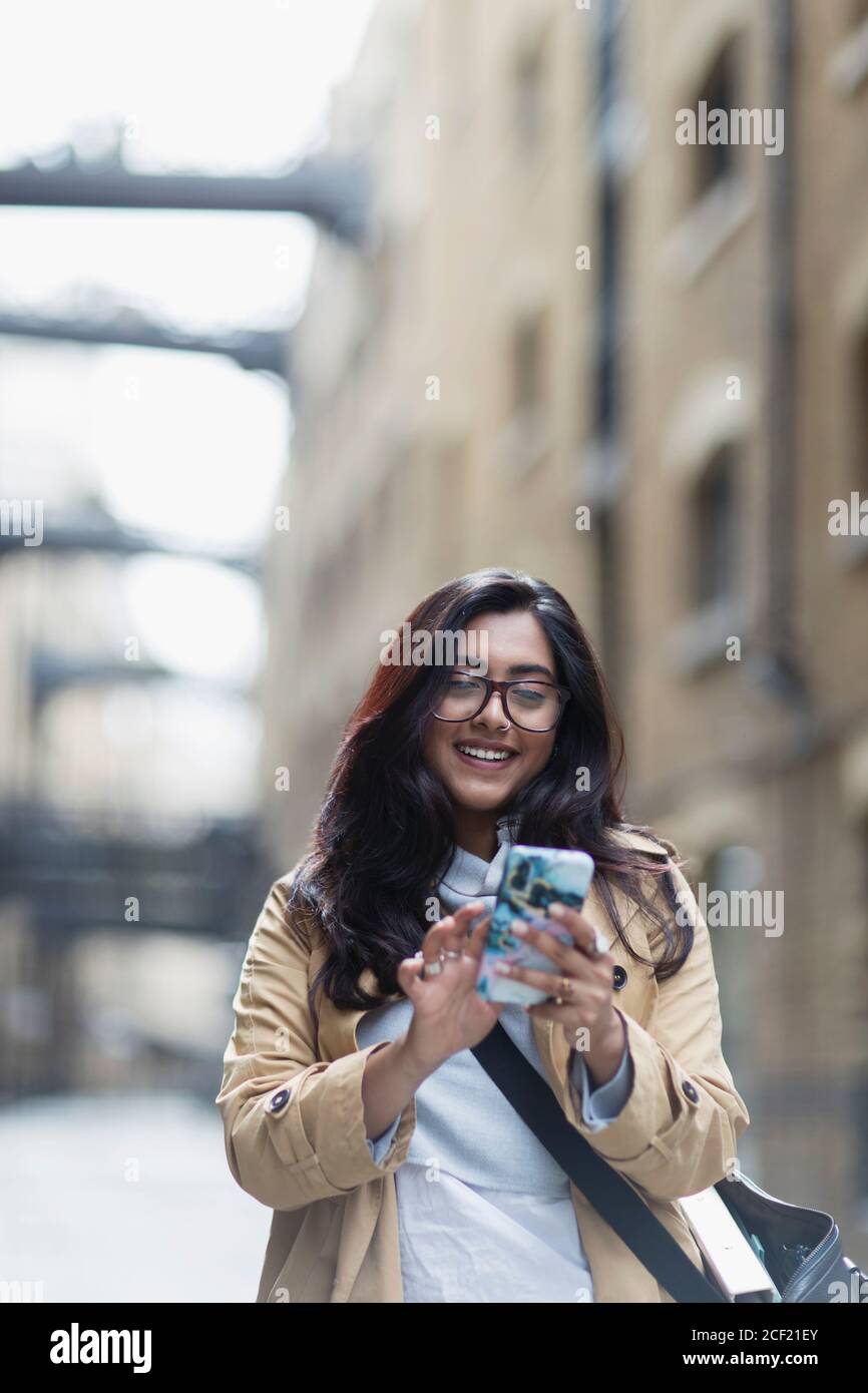 Donna sorridente che usa lo smartphone sul marciapiede Foto Stock