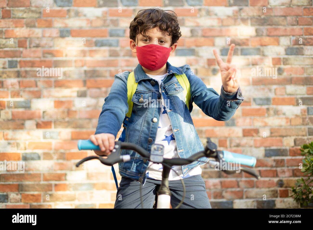 Ragazzo caucasico sulla sua moto pronto ad andare a scuola. Indossa una maschera facciale. Concetto di ritorno a scuola e nuova normalità. Foto Stock