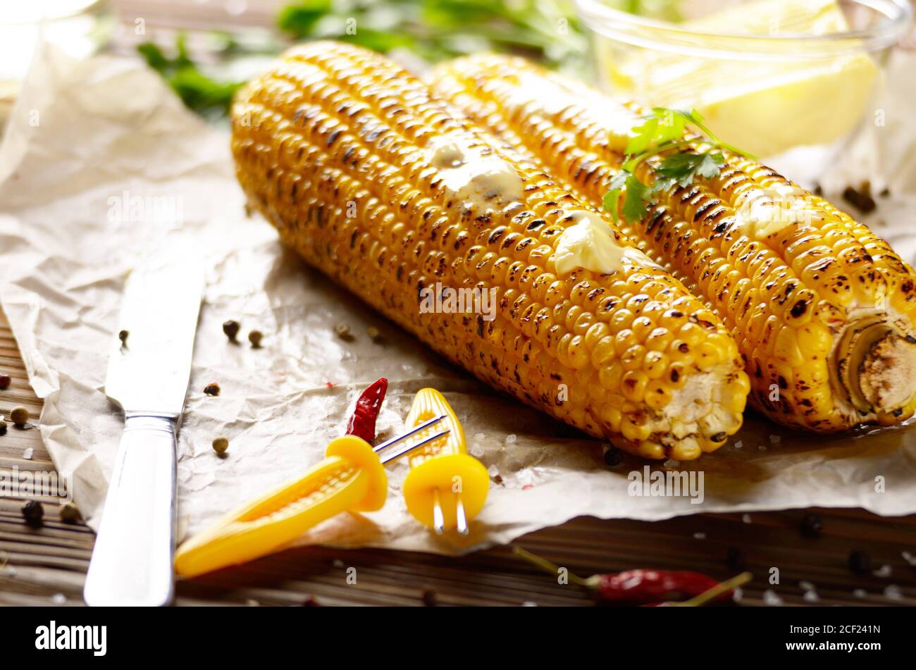 Tavolo da cucina con pannocchie di mais dolci alla griglia sotto burro di  fusione e verdi su carta da forno Foto stock - Alamy
