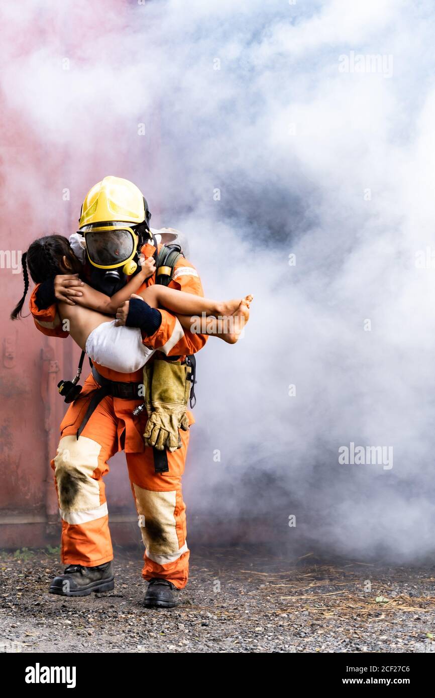 Pompiere salvataggio ragazza bambino piccolo da costruzione in fiamme. Tiene la ragazza e scava fuori attraverso il fumo dalla costruzione. Soccorso di sicurezza dei vigili del fuoco da Foto Stock