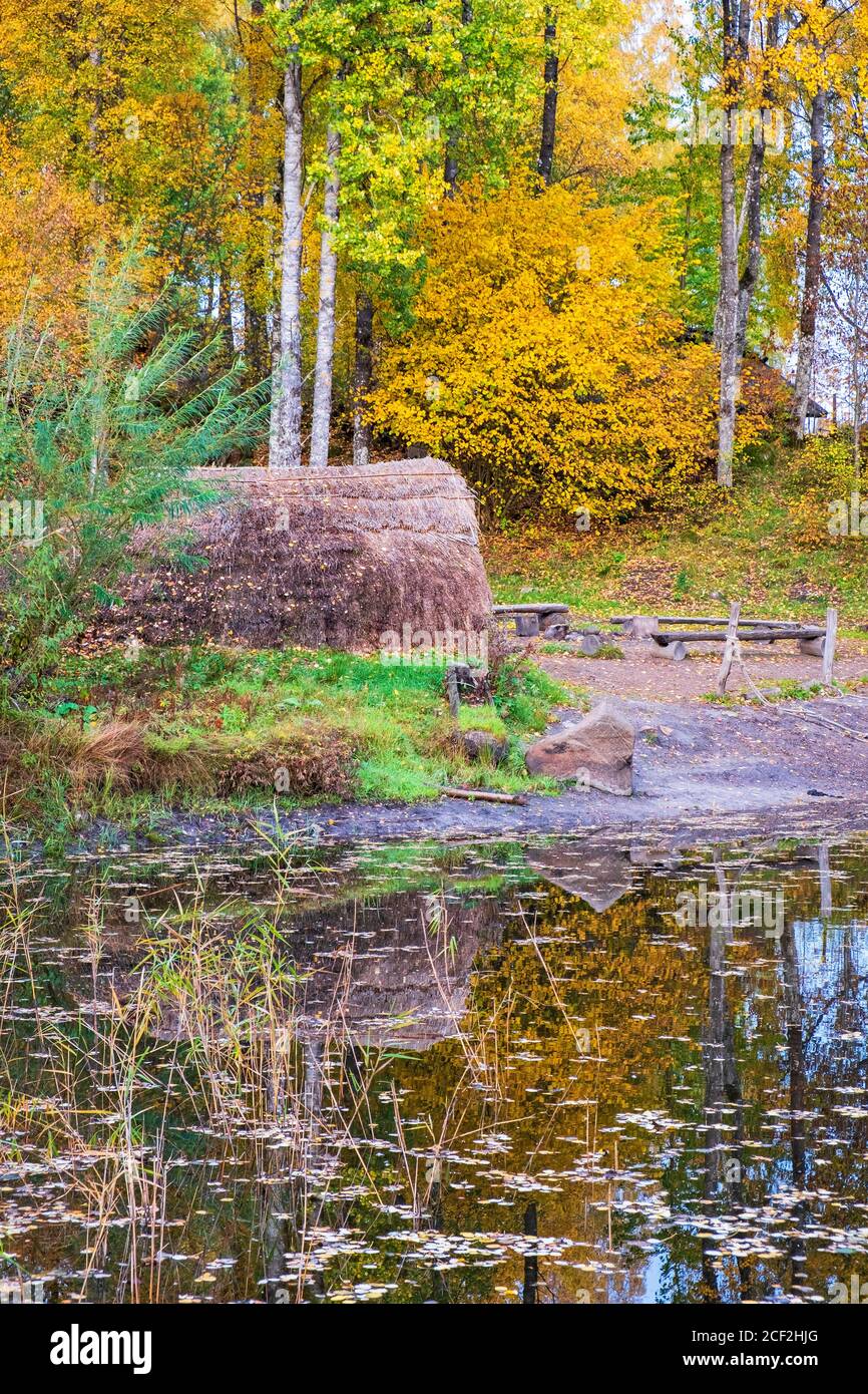 Capanna d'erba in un lago boschivo con colori autunnali, ricostruzione dell'epoca preistorica Foto Stock