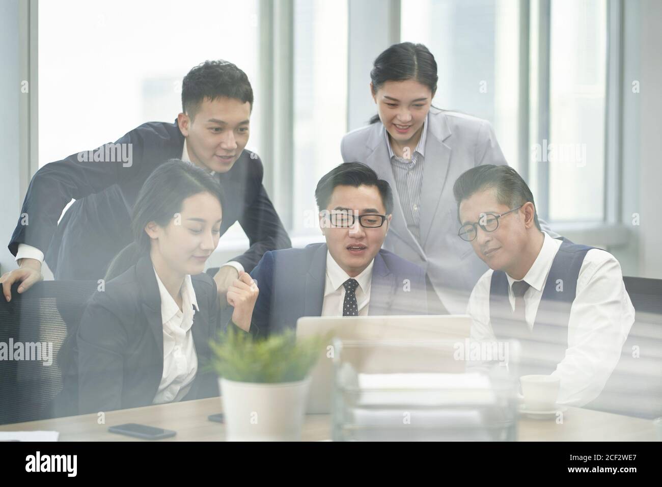 foto a tutto schermo del team di cinque dirigenti aziendali asiatici che si riunono in ufficio discutere di affari utilizzando un computer portatile Foto Stock