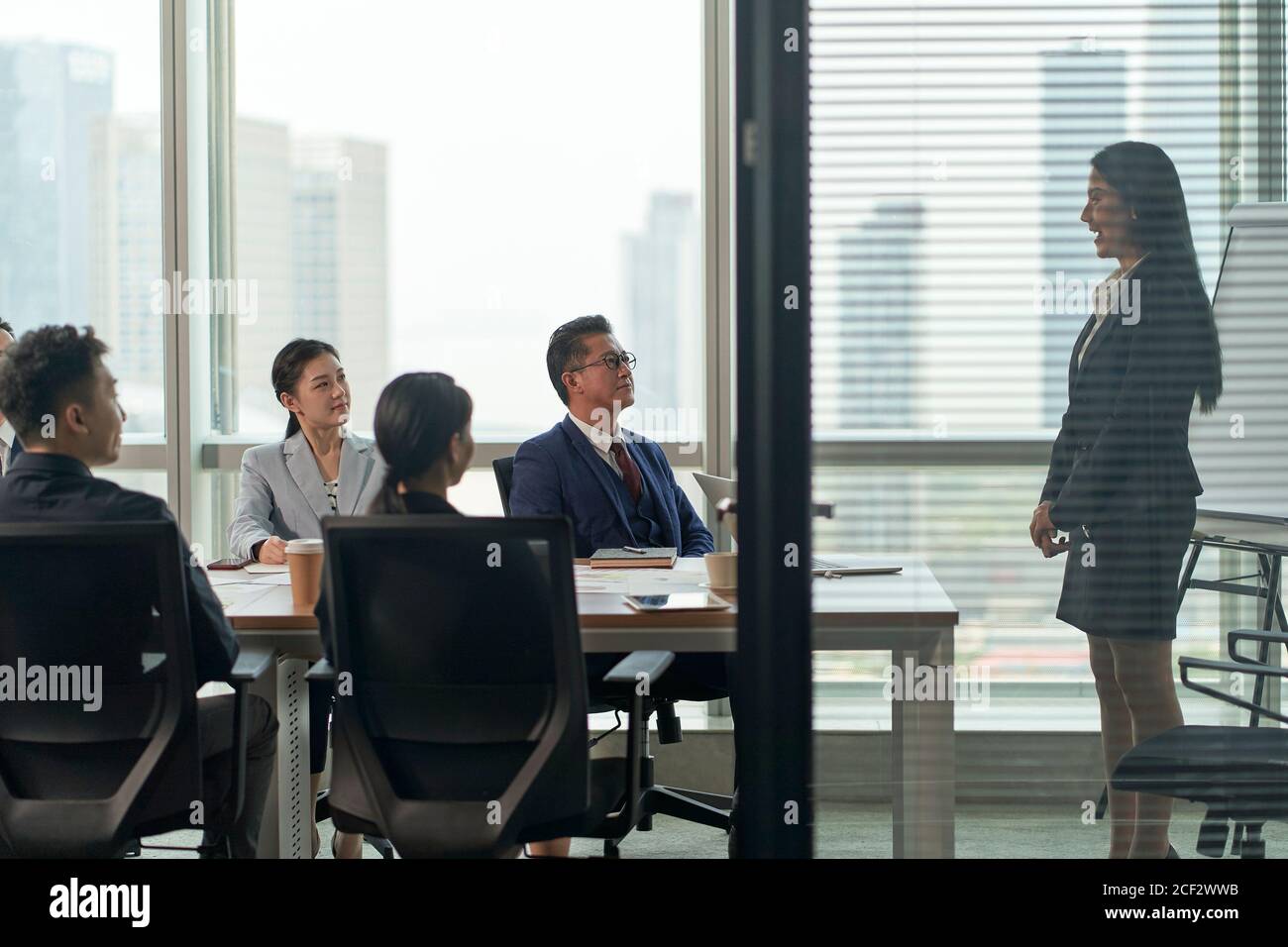 giovane donna d'affari asiatica che parla con un gruppo di uomini d'affari in riunione in sala conferenze Foto Stock