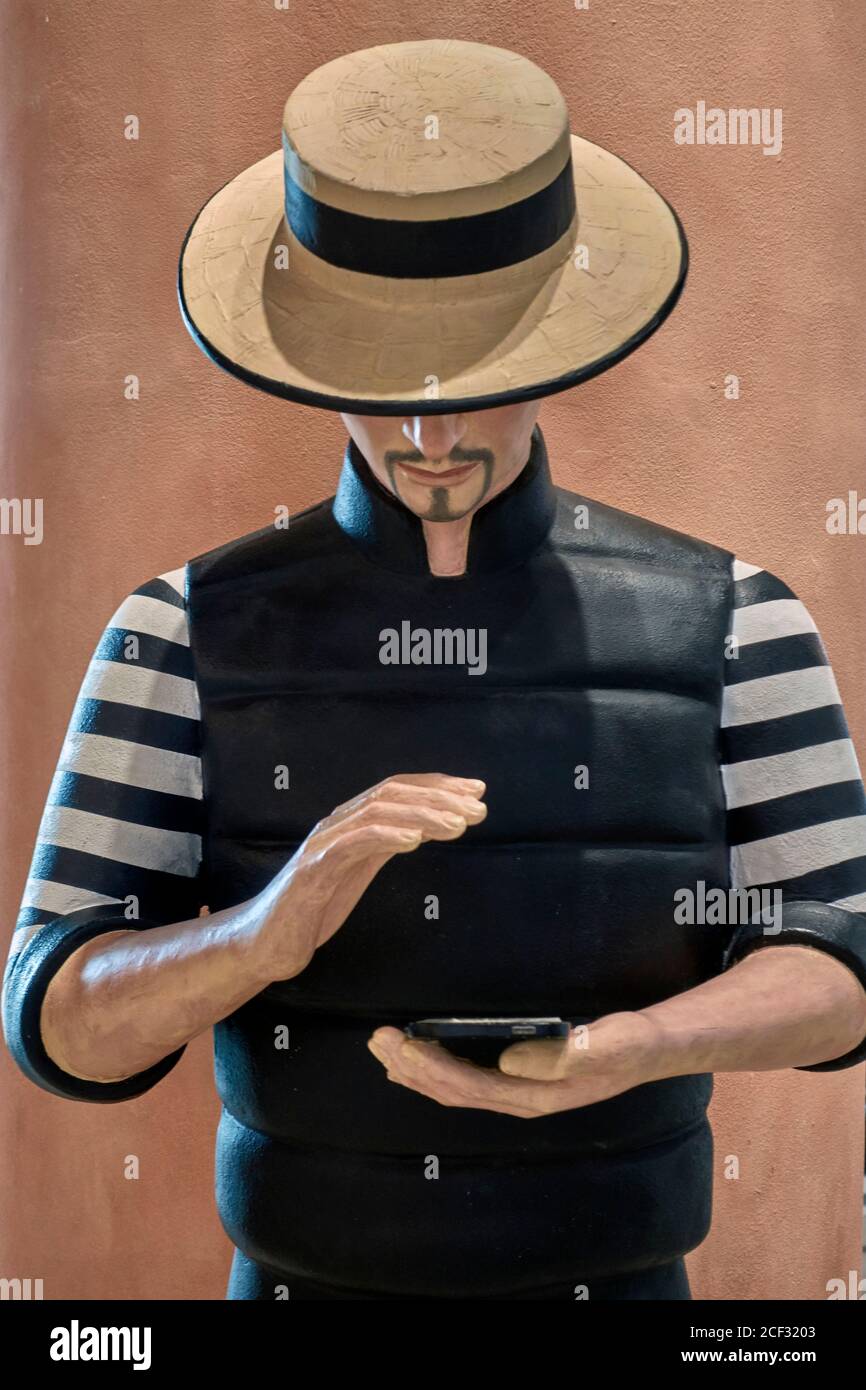 Statua di un uomo che guarda uno smartphone e vestito Come gondoliere veneziano con abiti tradizionali a righe e paglia cappello Foto Stock
