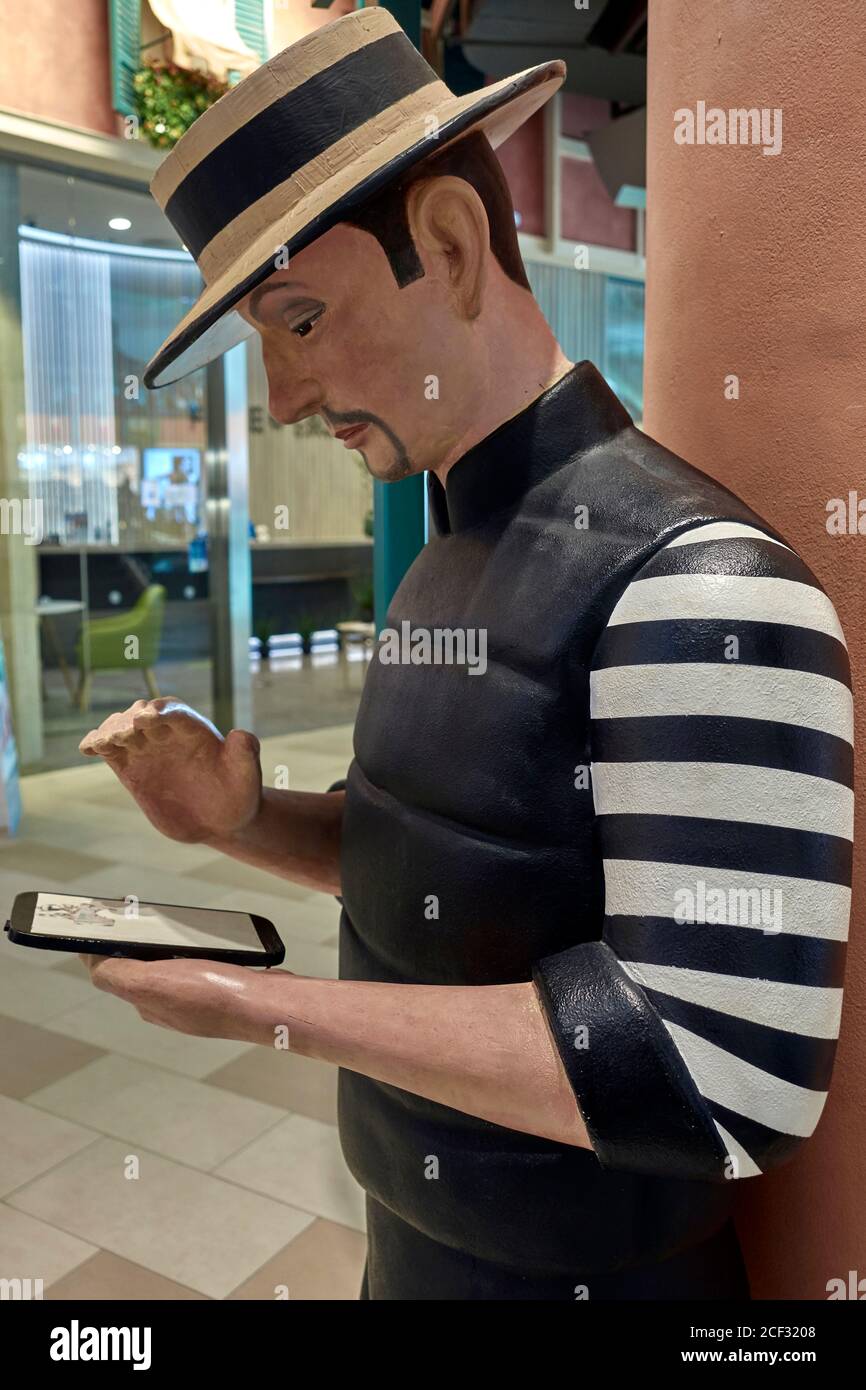 Statua di un uomo che guarda uno smartphone e vestito Come gondoliere veneziano con abiti tradizionali a righe e paglia cappello Foto Stock