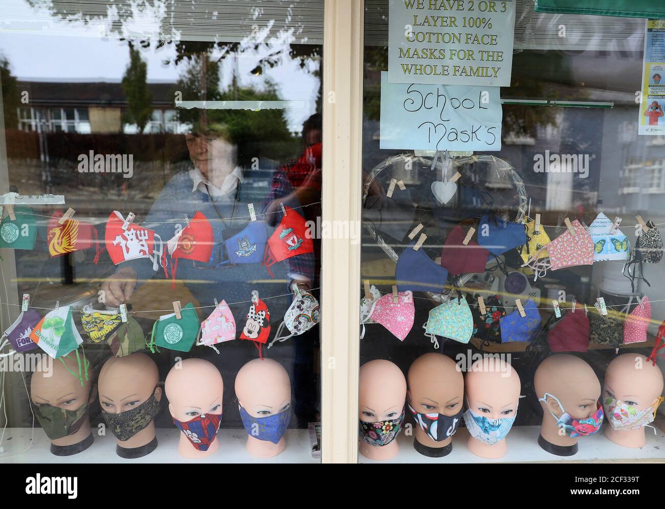 Gean D'Arcy, proprietario di Sew e zip Inn, Rathcoole, che hanno fatto maschere facciali nei colori delle uniformi scolastiche per soddisfare la domanda aumentata, regola la sua vetrina. Foto Stock