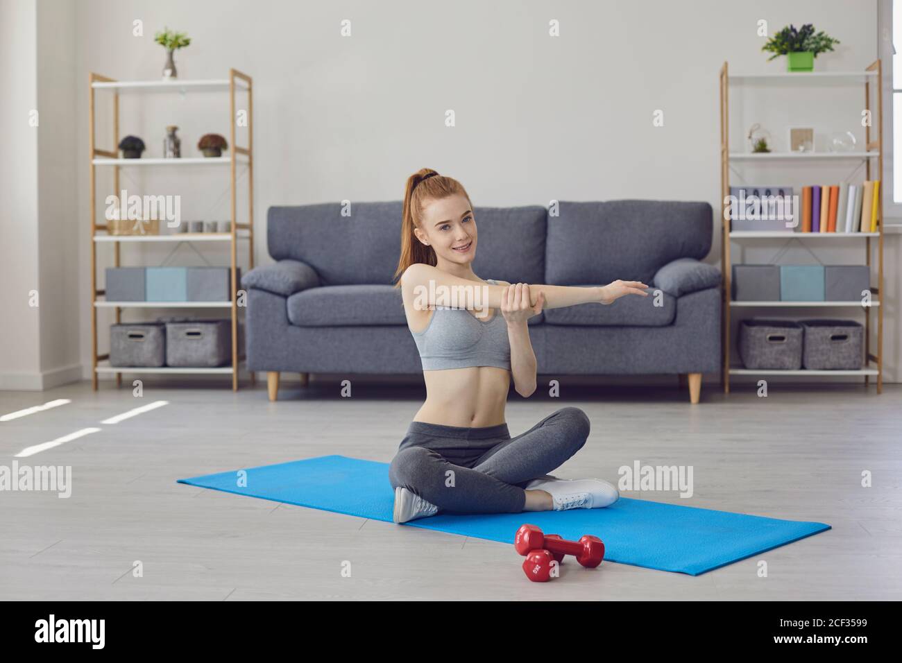 Giovane donna che allunga il braccio durante l'allenamento a casa Foto Stock