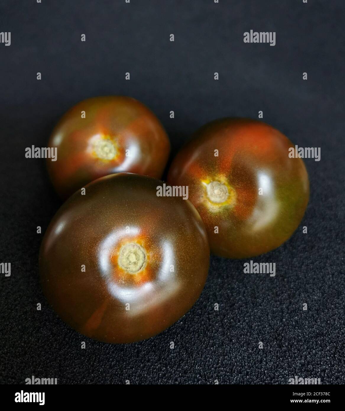 Tre pomodori freschi di colore rosso scuro su fondo nero Foto Stock