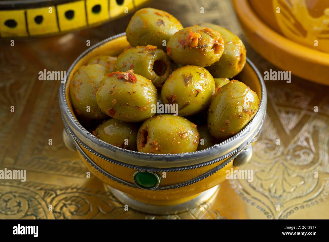 Olive tradizionali marocchine verdi speziate in una ciotola decorativa AS un piatto laterale su un tavolo di ottone Foto Stock
