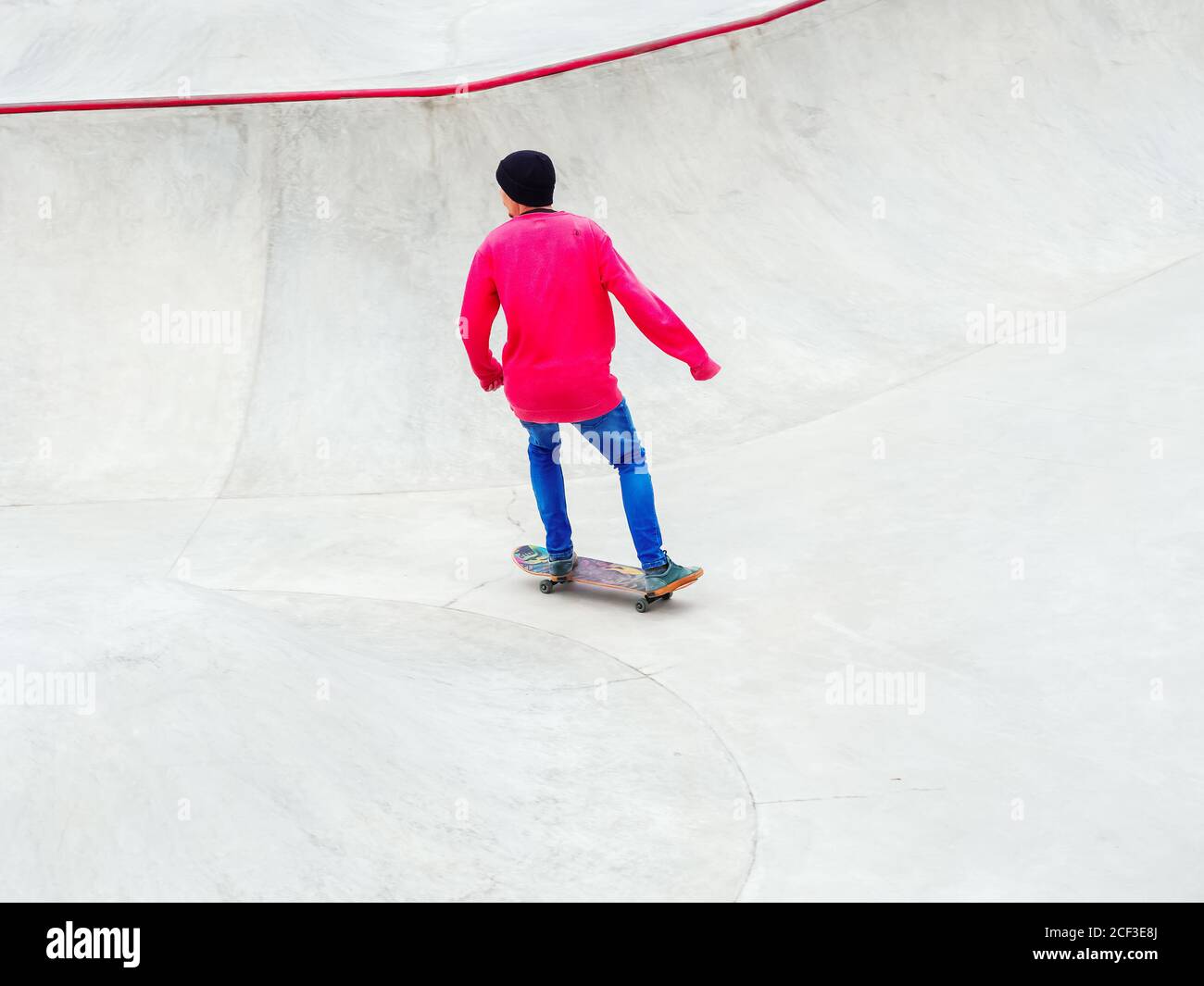 Un ragazzo con pantaloni blu e una felpa rosa cavalcano uno skateboard in  uno skatepark Foto stock - Alamy