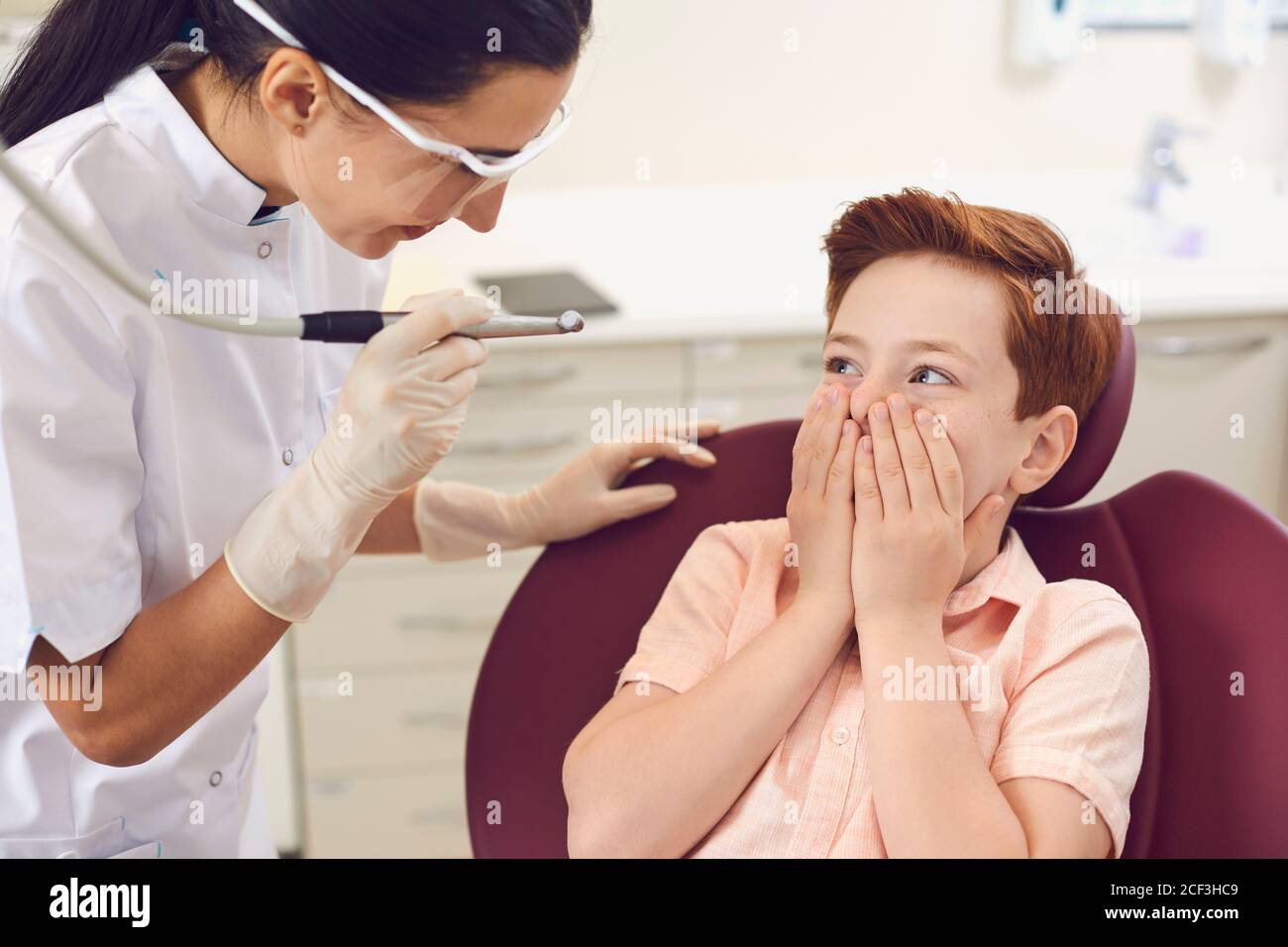 Clinica dentale. Ragazzo spaventato coprendo la bocca con le mani vicino al dentista Foto Stock