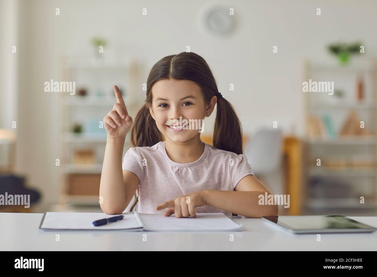 Sorridente ragazza seduta, imparando a contare e puntando una con il dito durante la lezione a casa Foto Stock