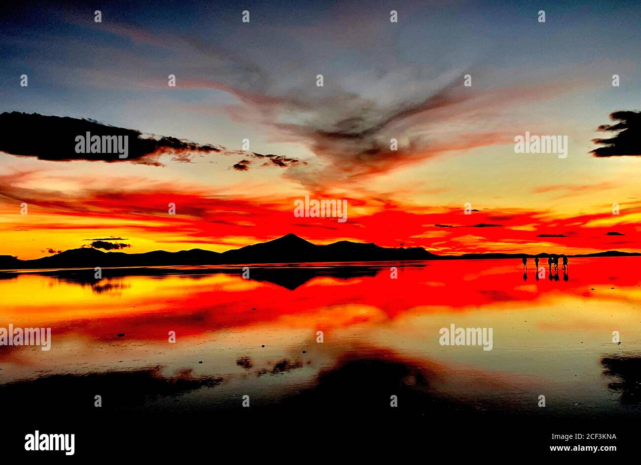 Bellissimo tramonto rosso sulle saline a Salar de Uyuni, Bolivia. Scenografia drammatica del cielo del tramonto. Riflessione nell'acqua del lago. Silhouette scure delle persone. Foto Stock