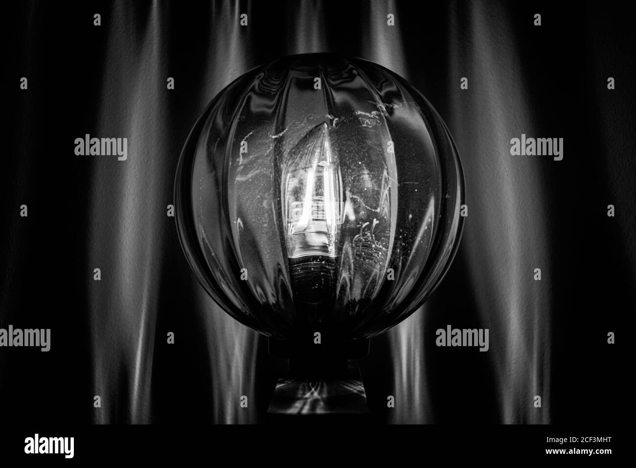 Bianco e nero. Design degli interni. Foto monocromatica della lampada con sfera rotonda e trasparente. Riflessione della luce sulla parete. Foto Stock