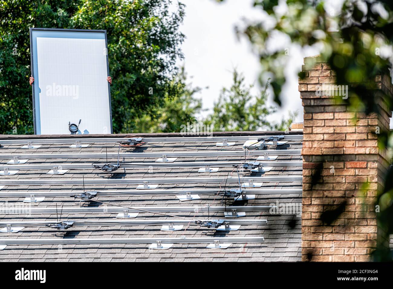 Installazione sul tetto lavoro con lavoratori che tengono pannelli solari con scaffalatura rack guide montate sulla parte superiore del tetto della casa residenziale per vivere fuori rete Foto Stock